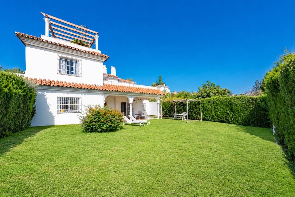 Fachada del chalet con jardín llano, porche cubierto y pérgola al fondo
