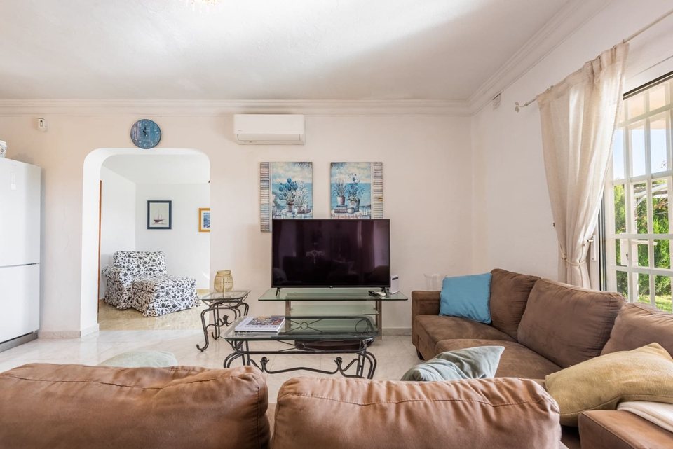 Salón con TV sobre mueble blanco, sofá en L marrón claro y mesa de centro