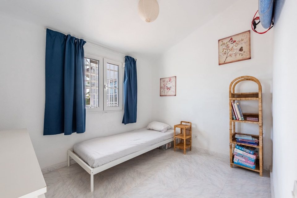 Dormitorio de matrimonio con cama blanca, cortinas azules y mesilla con lámpara