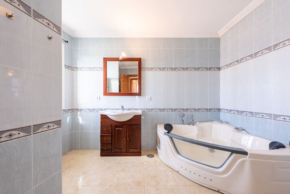 Baño con bañera hidromasaje, sanitarios blancos y mueble bajo lavabo de madera