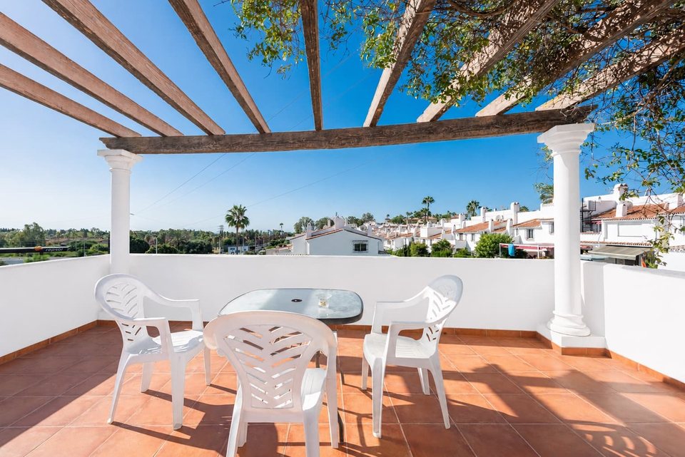 Porche cubierto con mesa y sillas de exterior, vistas al jardín y a la costa al fondo