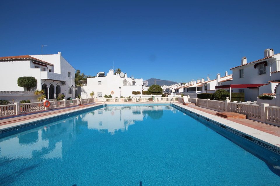 Piscina comunitaria con barandilla blanca, tumbonas y adosados alrededor