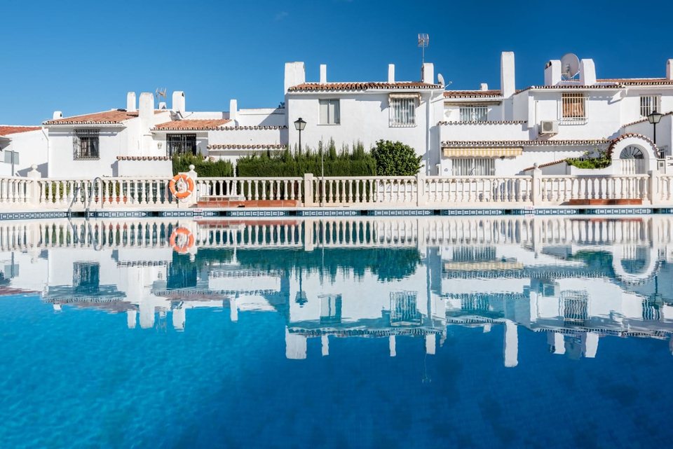 Piscina comunitaria grande con tumbonas y barandilla, adosados blancos alrededor