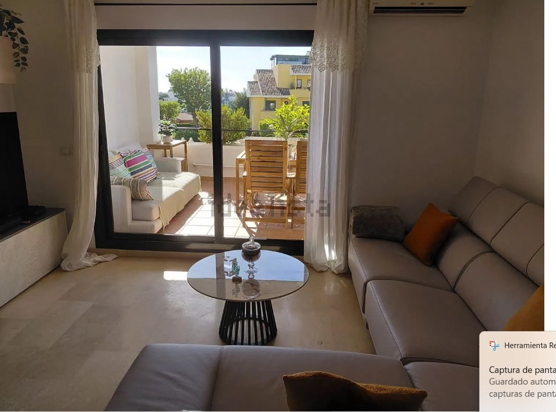 Salón-comedor visto desde el comedor con sofá gris, mesa de cristal redonda y cortinas blancas
