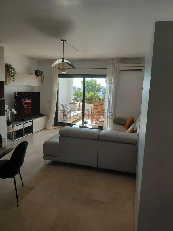 Salón-comedor en perspectiva amplia con sofá gris esquinero, mueble de televisión blanco y cortina blanca al ventanal