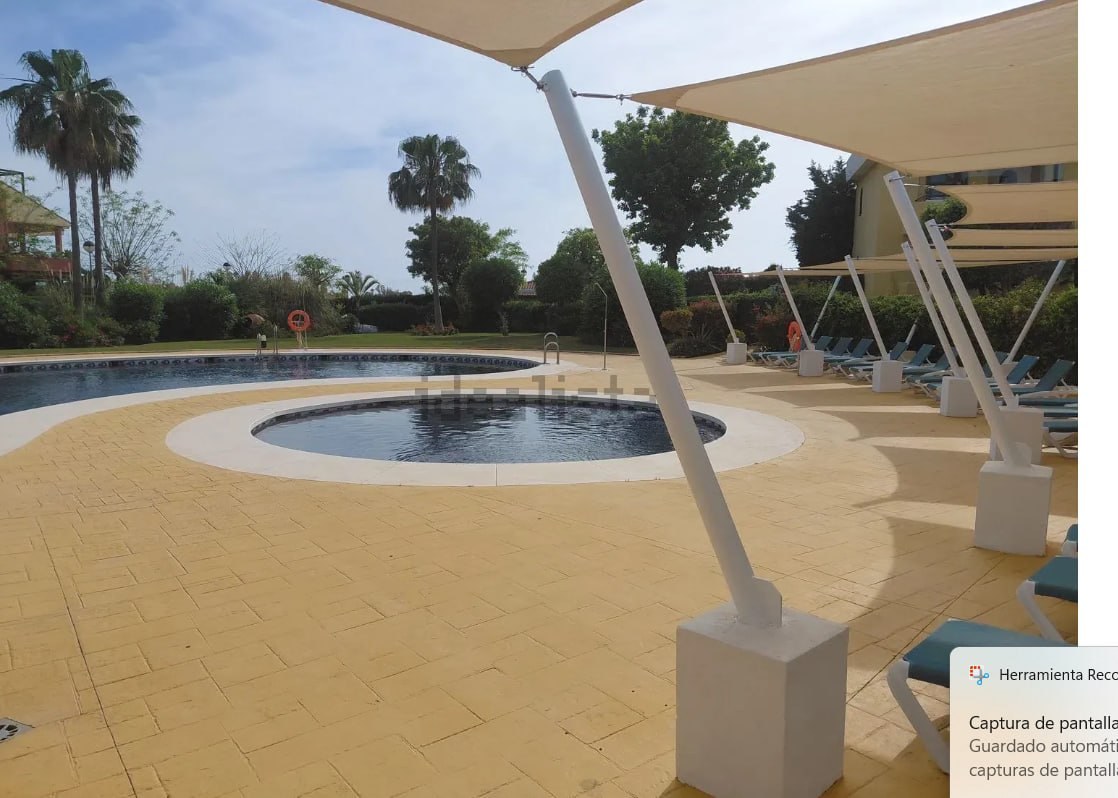 Piscina comunitaria con dos vasos, hamacas alineadas y sombrillas de tela blanca