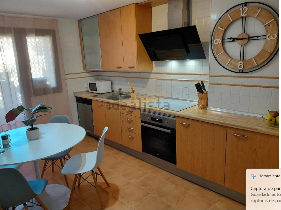 Cocina con muebles de madera clara, horno integrado, vitrocerámica y mesa blanca con sillas en el comedor diario