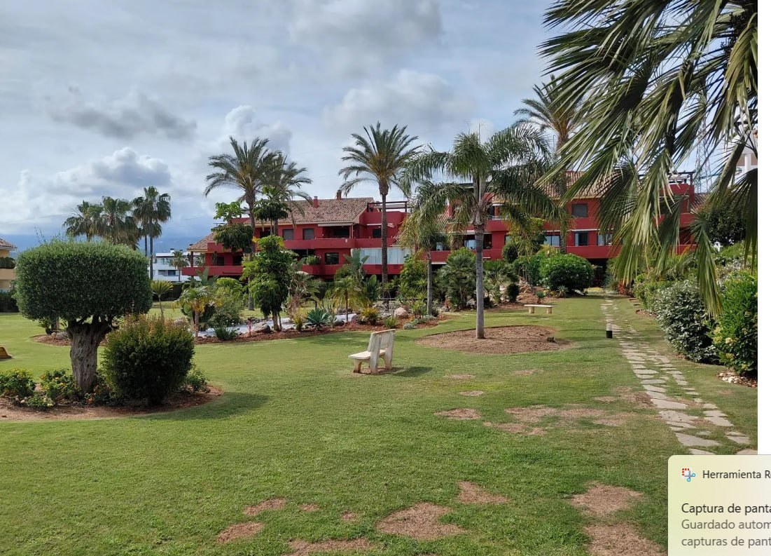 Jardines comunitarios con palmeras, camino empedrado y viviendas del conjunto al fondo